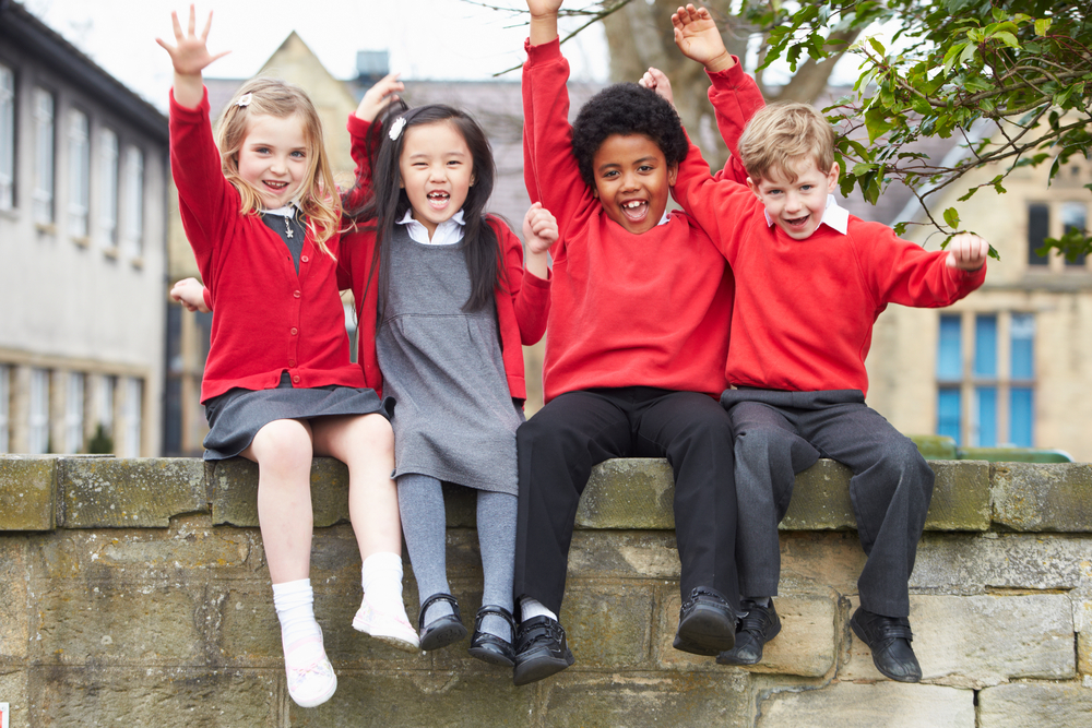 Happy children in school uniform sitting on wall with arms in the air